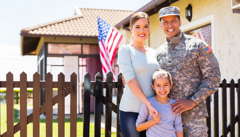 Military family posing outside of their home with american flag flying in background