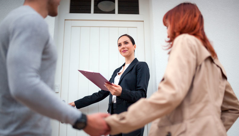 real estate agent opening the door for couple to view a home